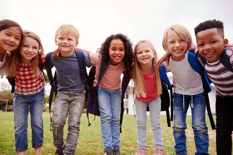 Excited elementary students with backpacks on playing on field at break time.