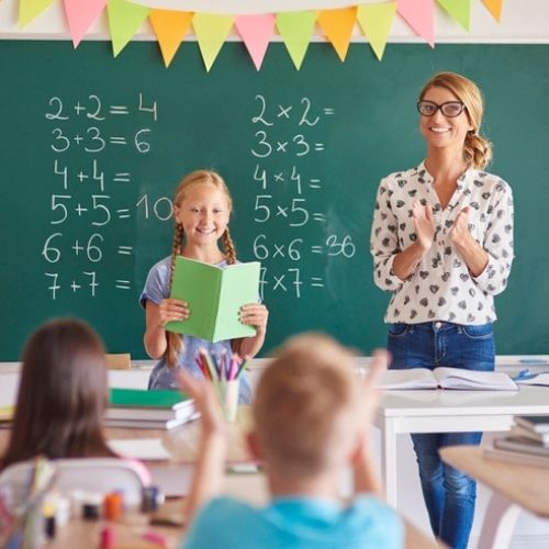 Elementary student in front of classroom with clapping teacher.